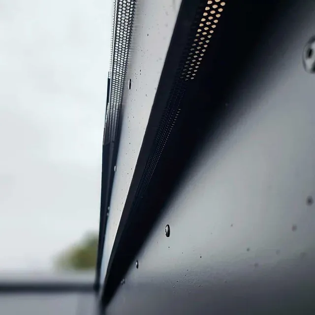Nærbilde av ventilasjonslist på fasade med regndråper på overflaten.