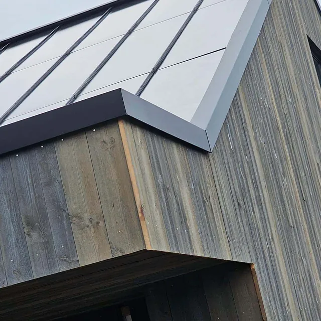 Sort tak med metallplater og beslag på hytte med værbitt trekledning.